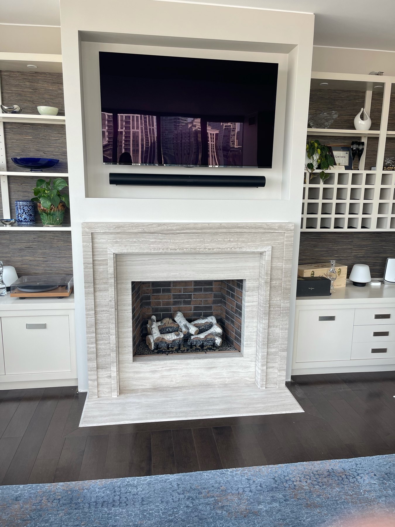 Finished light-stone fireplace below a television and surrounded by custom built-ins
