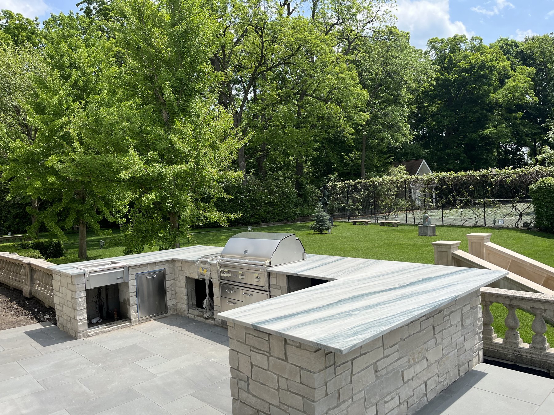Large outdoor kitchen with pale blue-green stone counters overlooking a landscaped yard